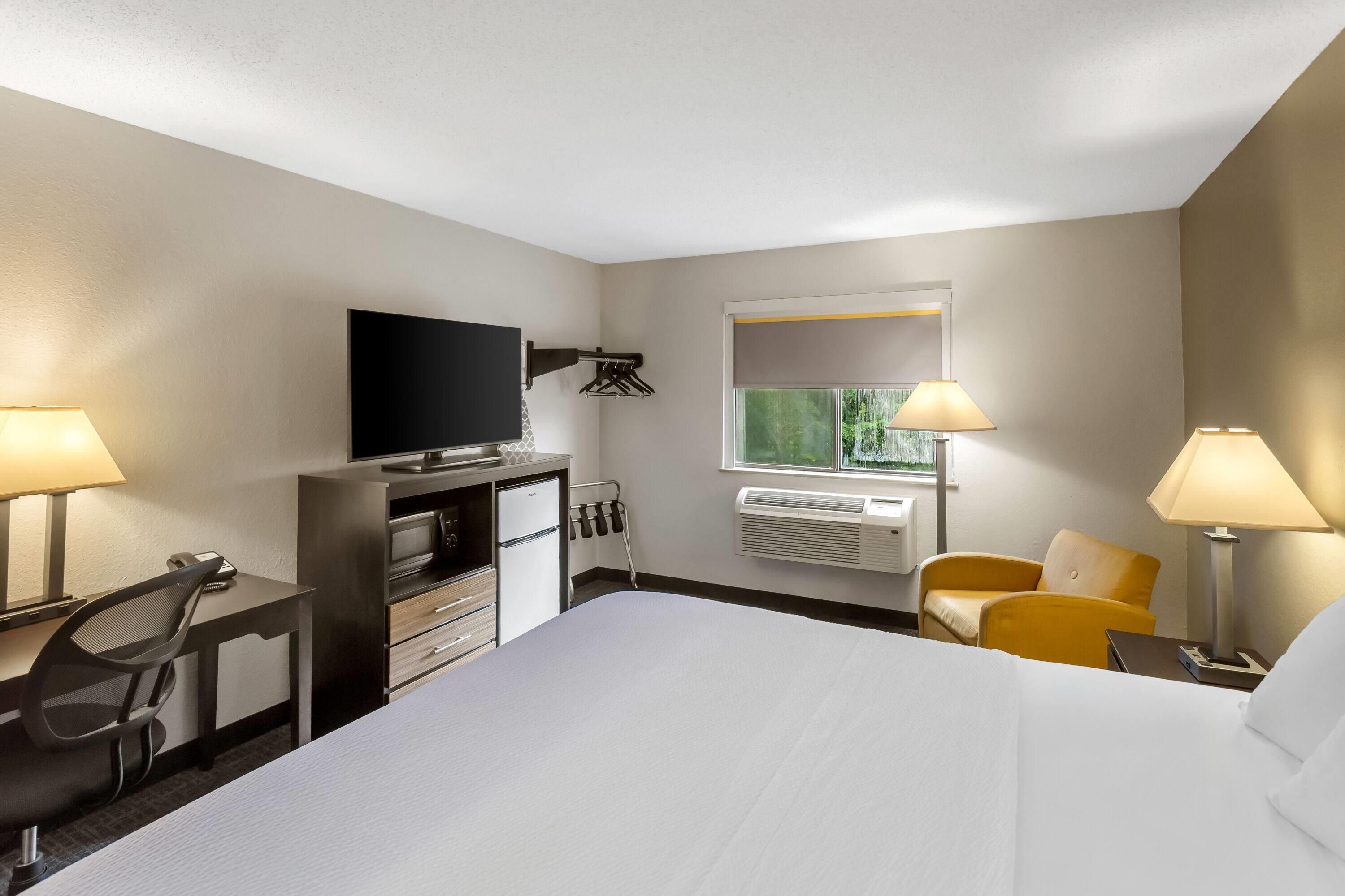 Quarto de hotel com cama, escrivaninha com televisão de tela plana, minibar, cadeira, janela com vista e duas luminárias.