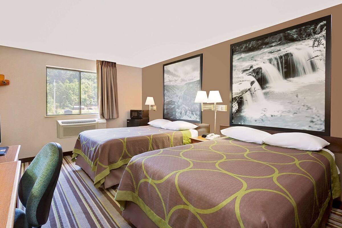 A hotel room with two beds, a desk, a chair, a TV, and a window with curtains.