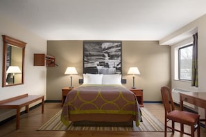 A hotel room with a large bed, two bedside tables with lamps, a chair, a desk, a mirror, and a large wall-mounted artwork.