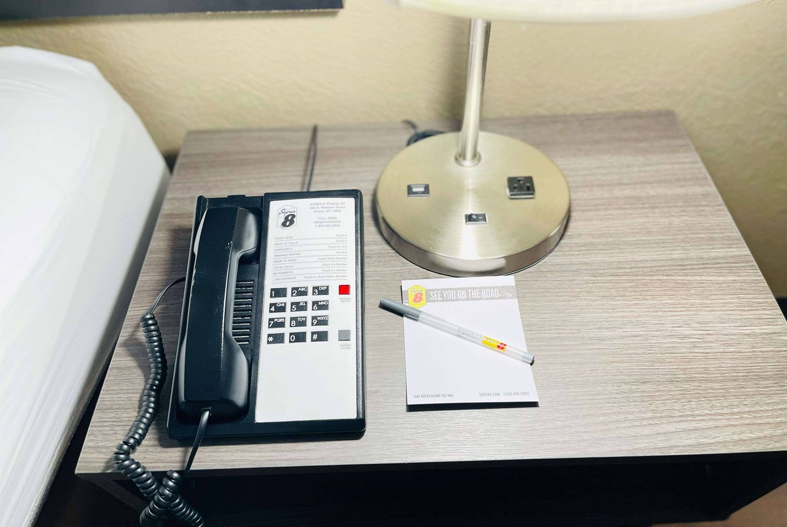 Une chambre d’hôtel avec une table de chevet sur laquelle se trouvent un téléphone noir, une lampe et un bloc-notes avec un stylo.