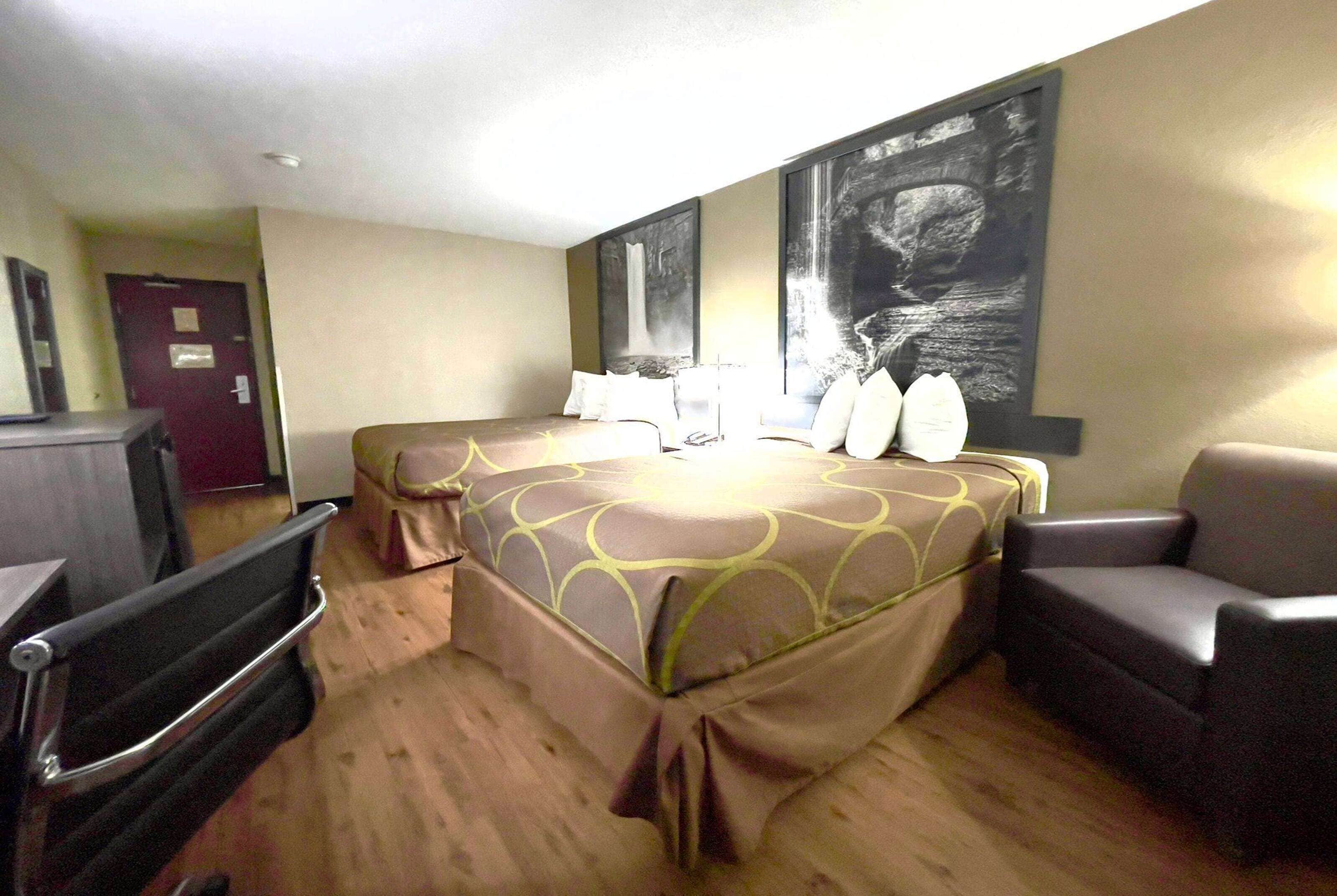 A hotel room with a bed, two chairs, a desk, and a door.