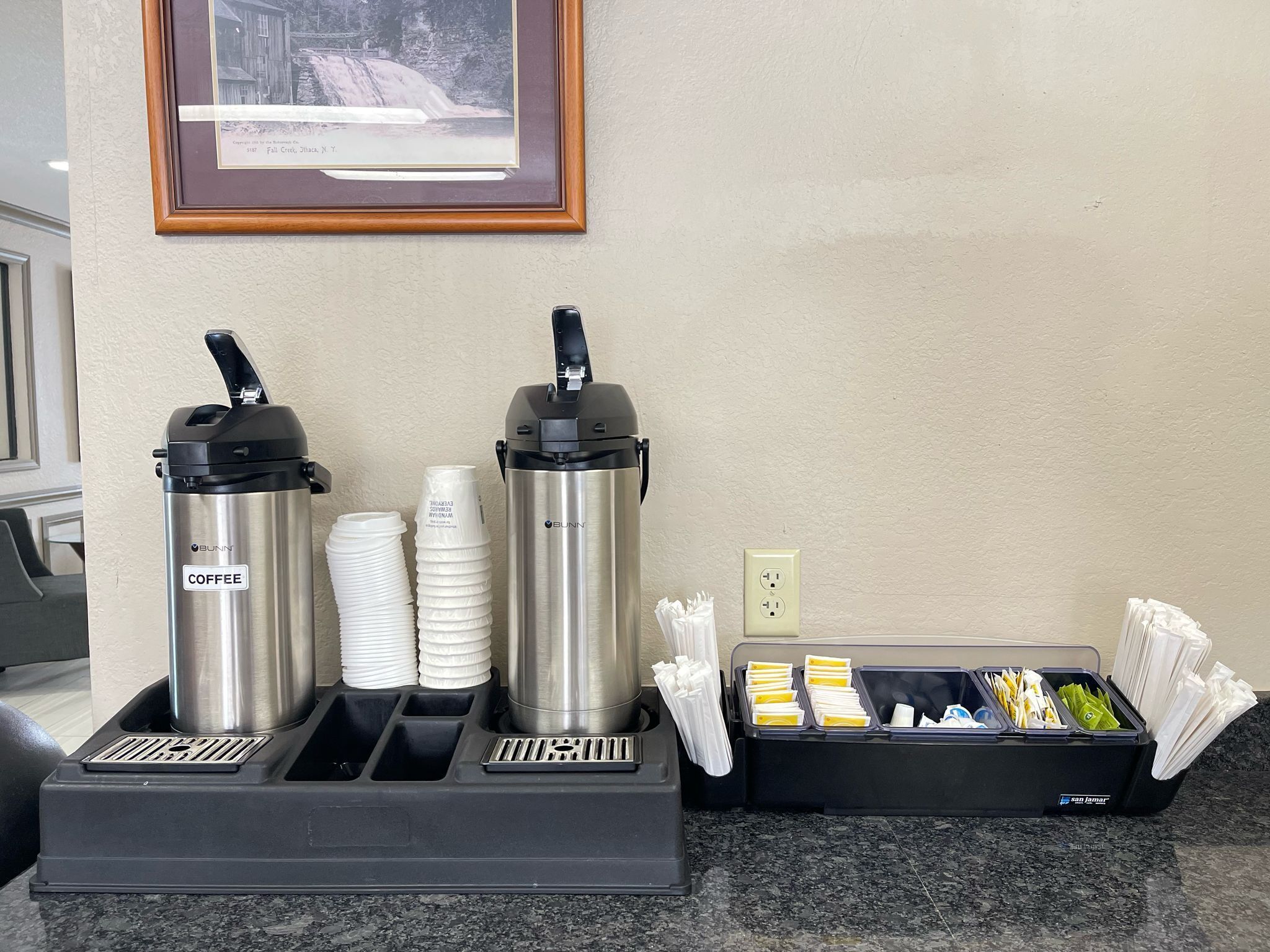 A coffee station with two coffee makers and a container of napkins.
