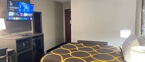 Quarto de hotel com uma cama, uma mesa com uma TV, um abajur e um telefone.