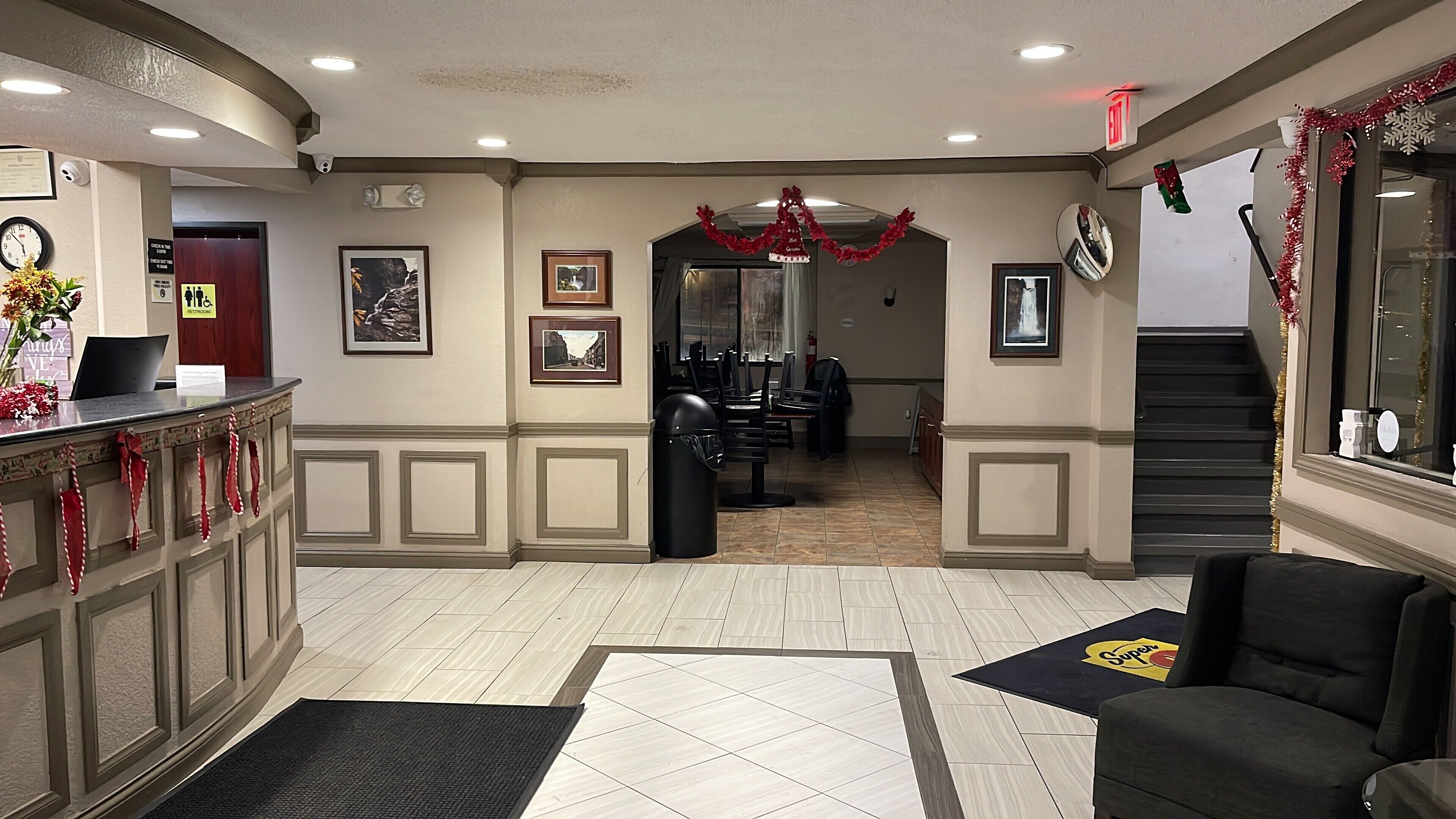 A hotel lobby with a reception desk, framed pictures on the walls, a staircase, and a Christmas decoration.