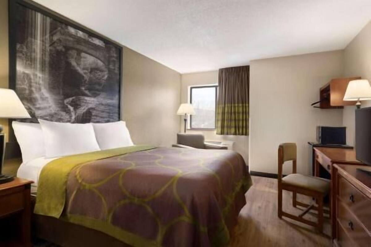 A hotel room with a bed, a desk, a chair, a television, and a large window.