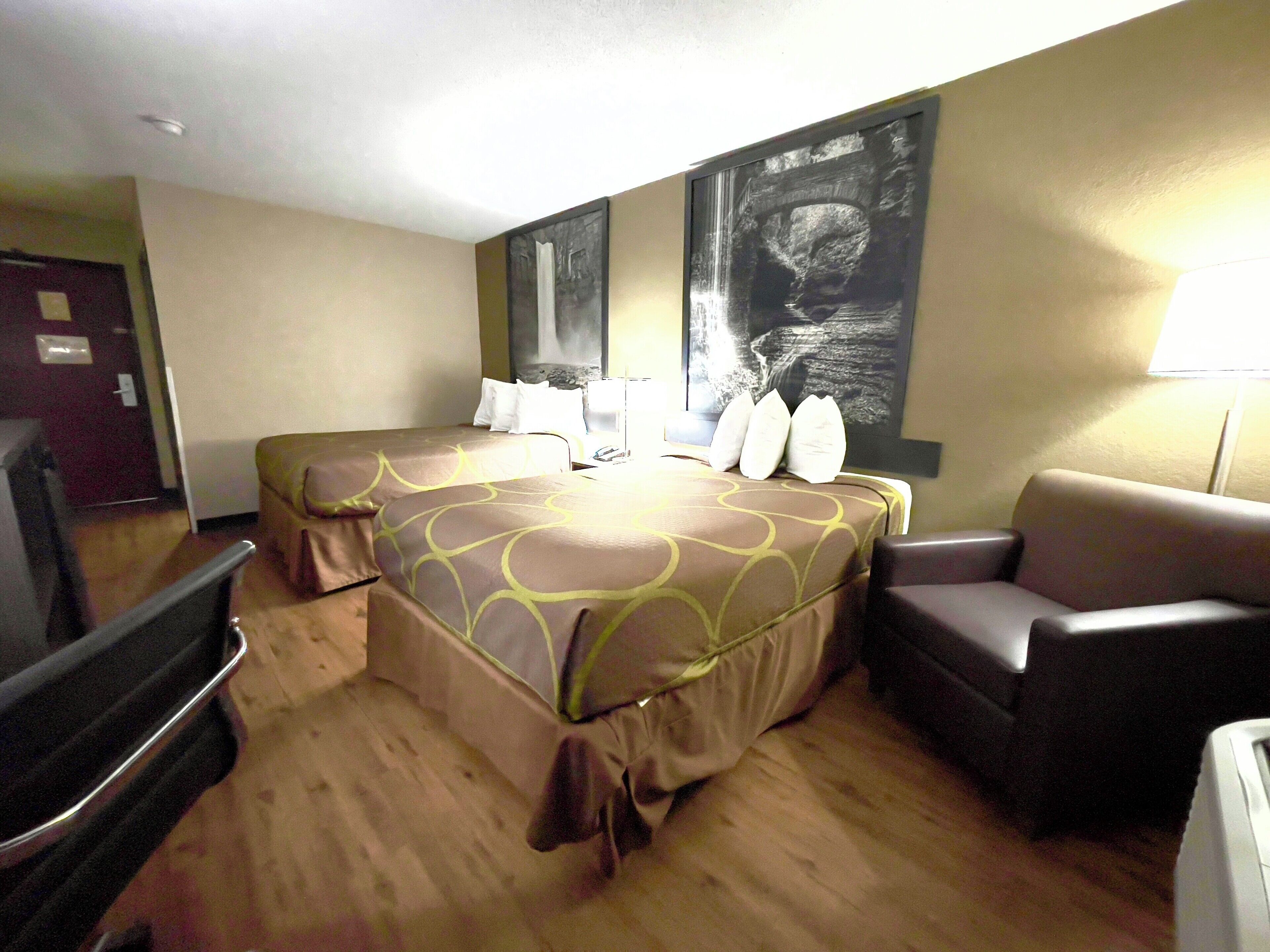 A hotel room with two beds, a sofa, a desk, and a large painting on the wall.