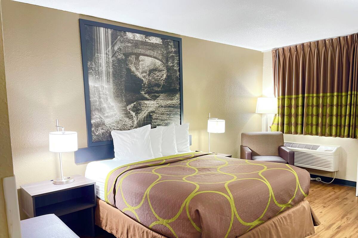 A hotel room with a bed, a desk, a chair, a lamp, and a large wall mural.