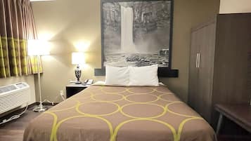 A hotel room with a bed, a nightstand with a lamp, a painting of a waterfall, and a wardrobe.