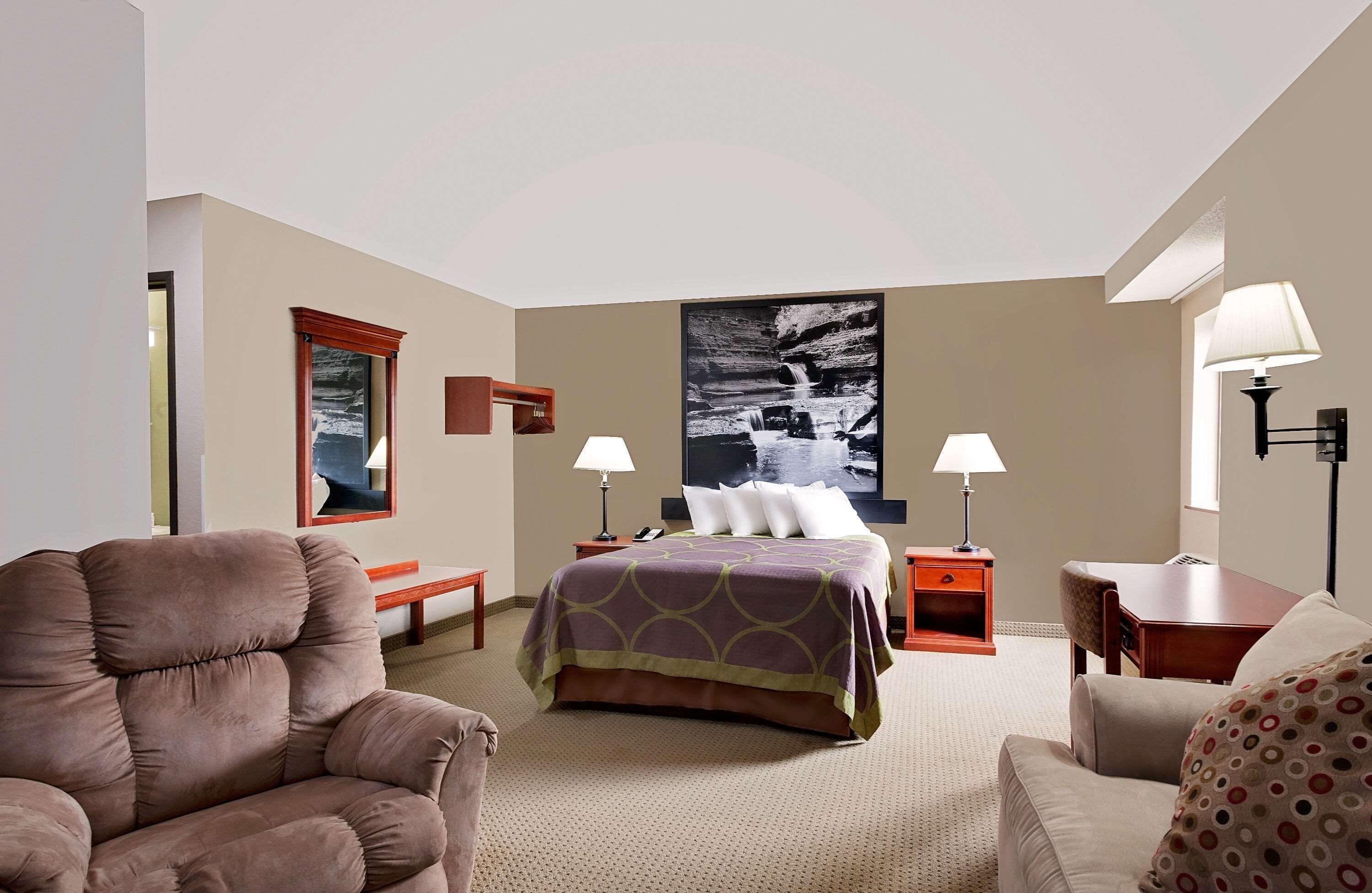 Une chambre d’hôtel comprenant un lit, deux tables de chevet, une chaise, un bureau et un grand tableau accroché au mur.