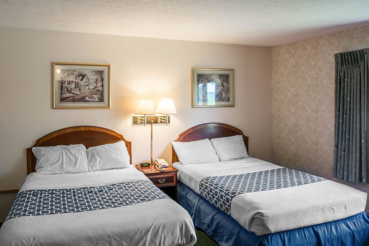 A hotel room with two beds, a nightstand with a lamp, and two framed pictures on the wall.