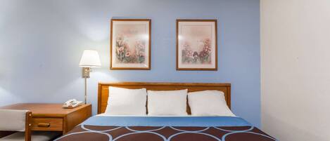 A hotel room with a bed, a bedside table with a lamp, and two framed pictures on the wall.