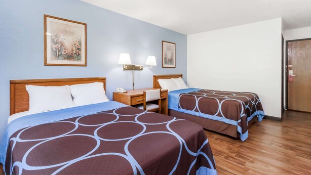 A hotel room with two beds, a desk with a lamp, and a door.