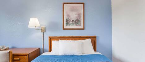 A hotel room with a bed, a desk with a lamp, and a framed picture on the wall.