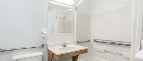 Un baño pequeño y blanco con tocador de madera, inodoro, lavamanos y ducha.