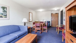 A compact room with a blue sofa, wooden dining table, chairs, a TV, and a kitchenette.