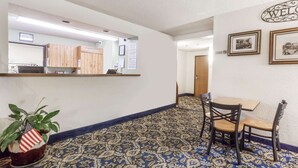 A reception area with a reception desk, a small table with chairs, a potted plant, and framed pictures on the wall.