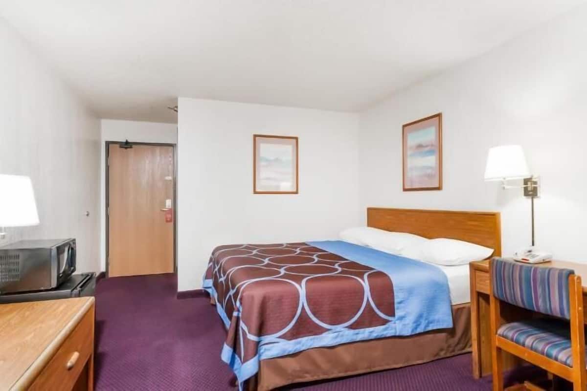 A hotel room with a bed, a desk, a chair, a television, and two wall-mounted lamps.