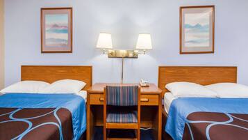 Een hotelkamer met twee bedden, een bureau met stoel, een lamp en twee foto's in lijsten aan de muur.