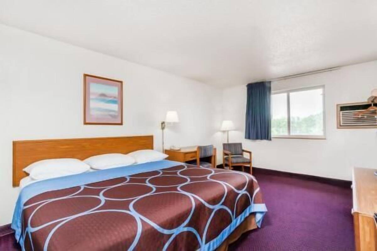 A hotel room with a bed, desk, chair, and a window with curtains.