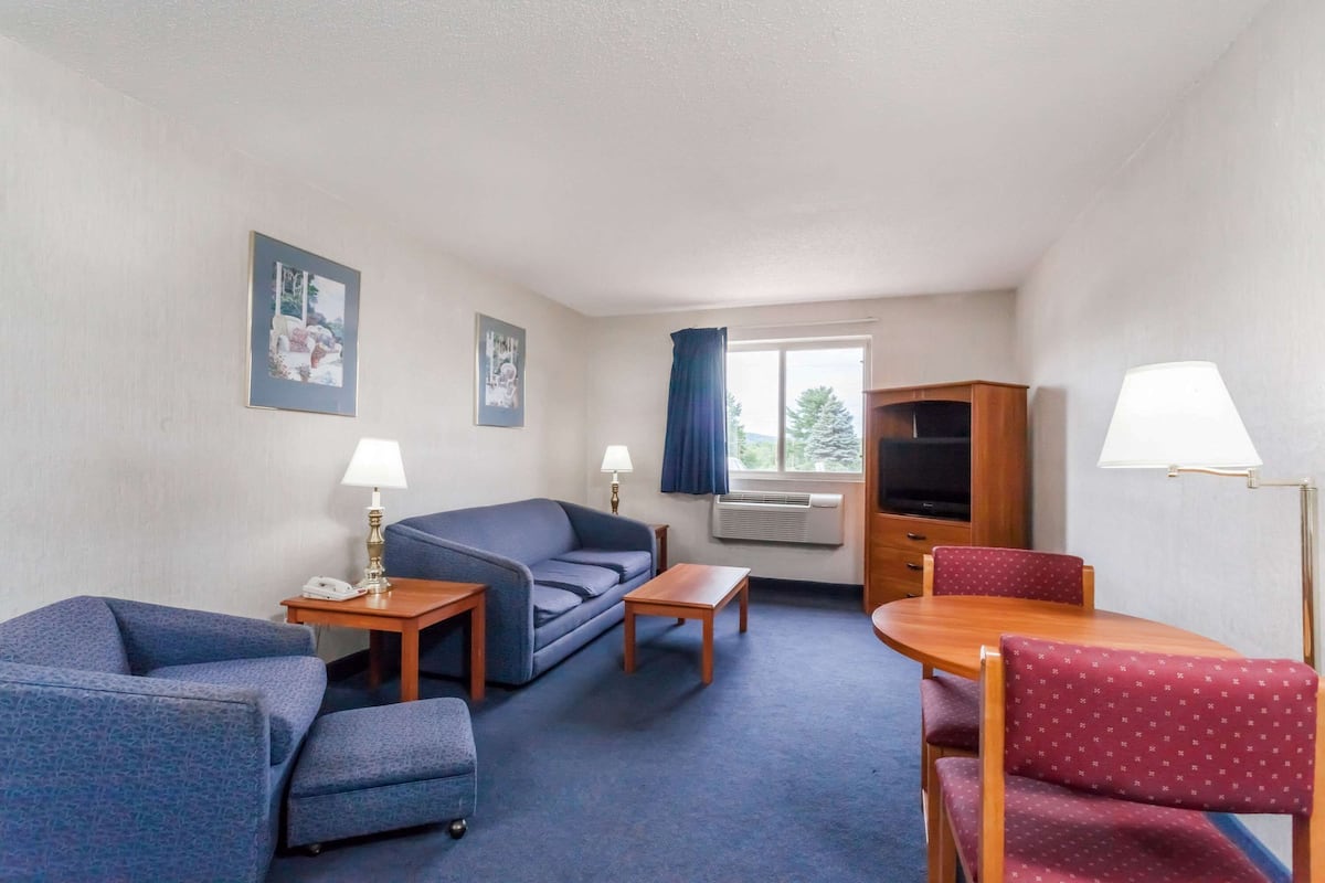 A hotel room with a blue carpet, a sofa, a small table, a wooden cabinet, and a dining table with chairs.