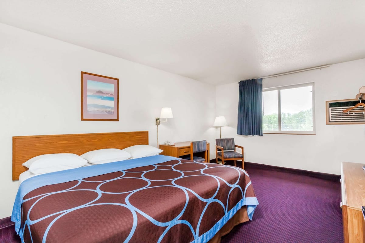 A hotel room with a large bed, two bedside tables, a desk, a chair, and a window with curtains.