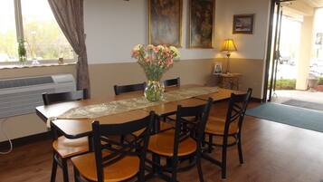 A dining area with a wooden table, four chairs, a vase of flowers, and two paintings on the wall.