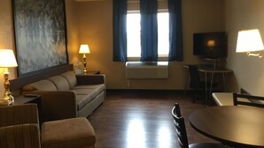 Quarto de hotel com sofá, mesa de jantar, televisão e janela com cortinas.