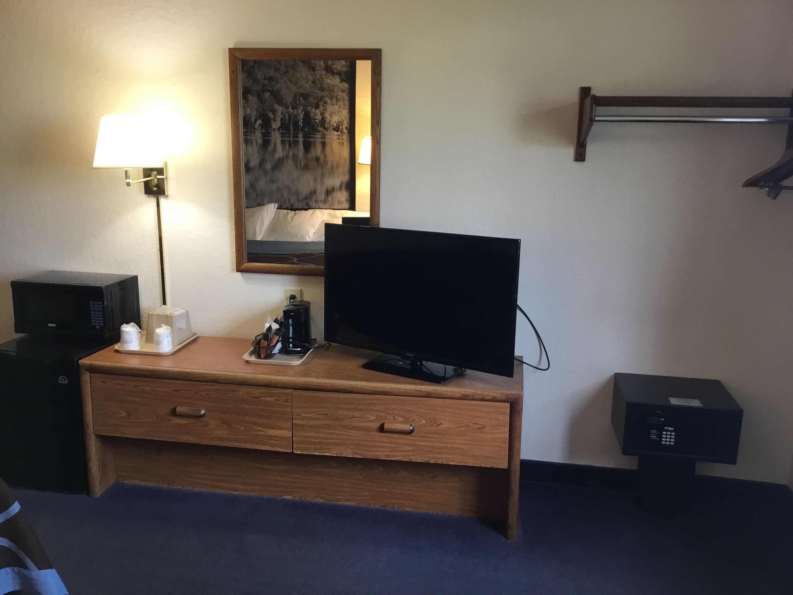 Una habitación de hotel con un escritorio de madera, un televisor de pantalla plana, una lámpara, una cafetera y un mueble pequeño.