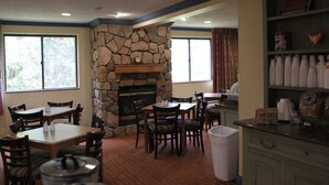 A dining area with a stone fireplace, wooden tables and chairs, and a view of the outdoors through large windows. - Quality Inn Cortland - University Area (Cortland)