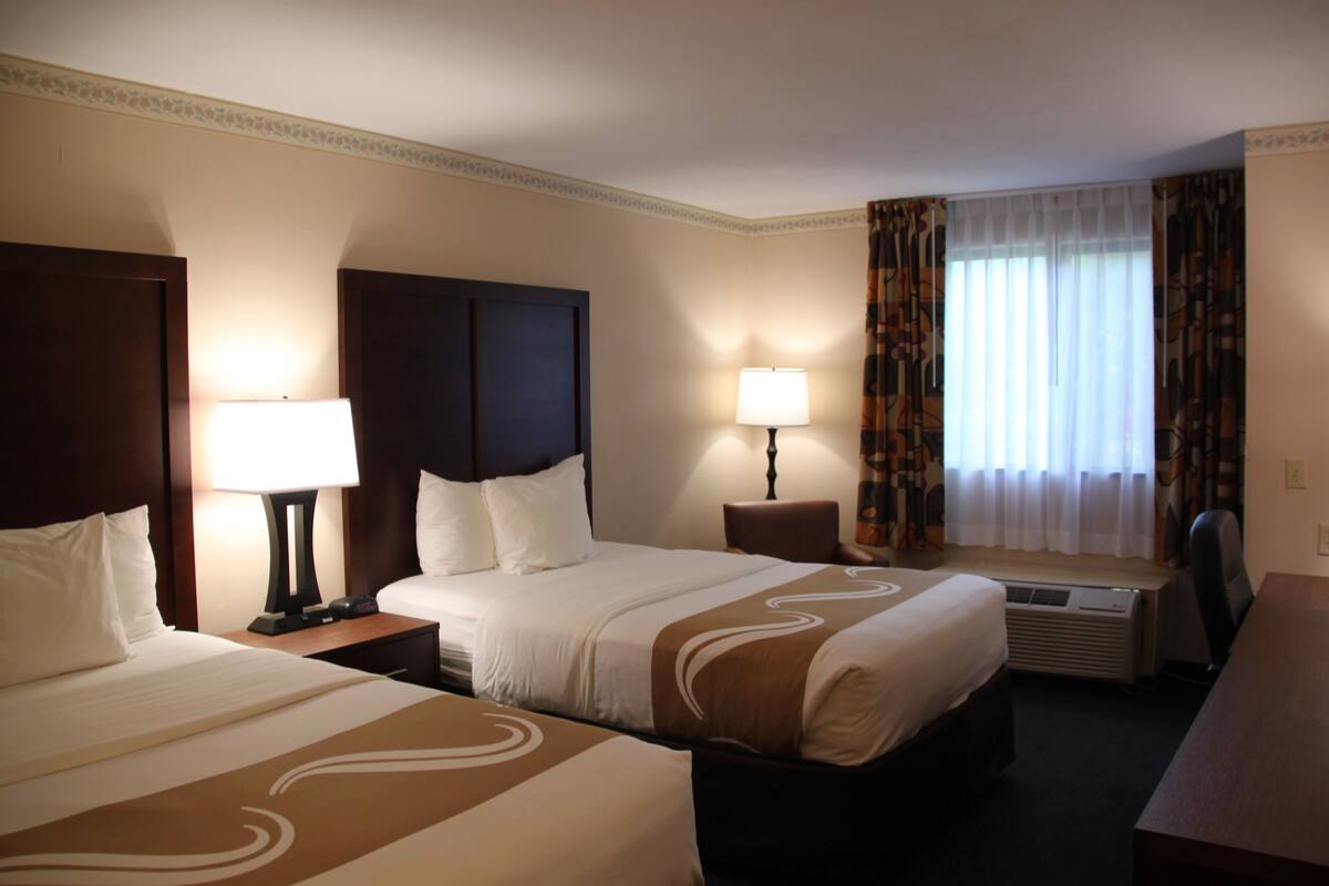 A hotel room with two beds, a desk, and a window with curtains.
