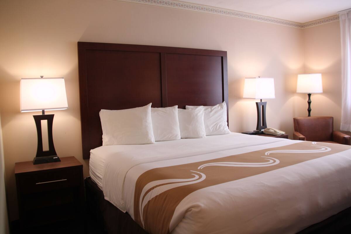 A hotel room with a large bed, two bedside tables with lamps, a chair, and a nightstand with a phone.