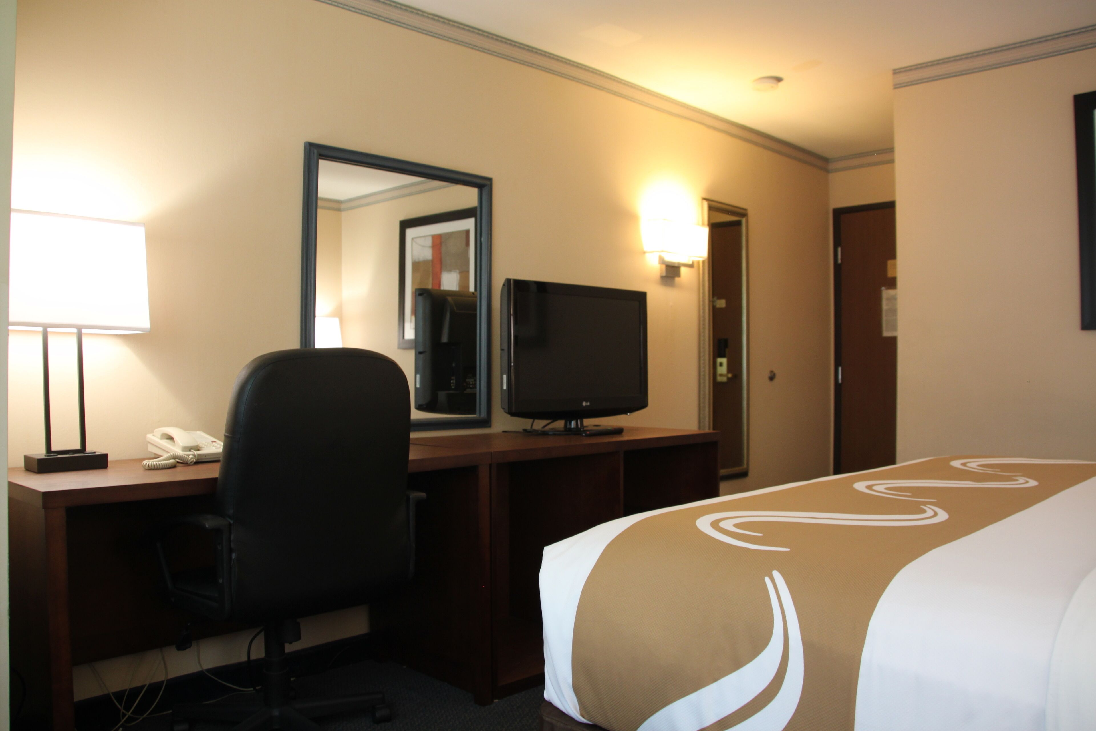 A hotel room with a bed, desk, chair, television, and a mirror.