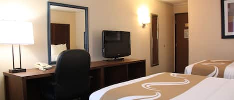 A hotel room with a desk, a television, a mirror, and two beds with decorative bedspreads.