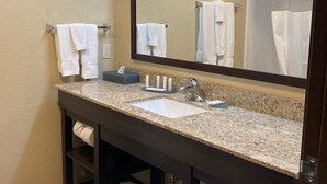Un baño con un espejo grande, un lavamanos y un perchero para toallas.