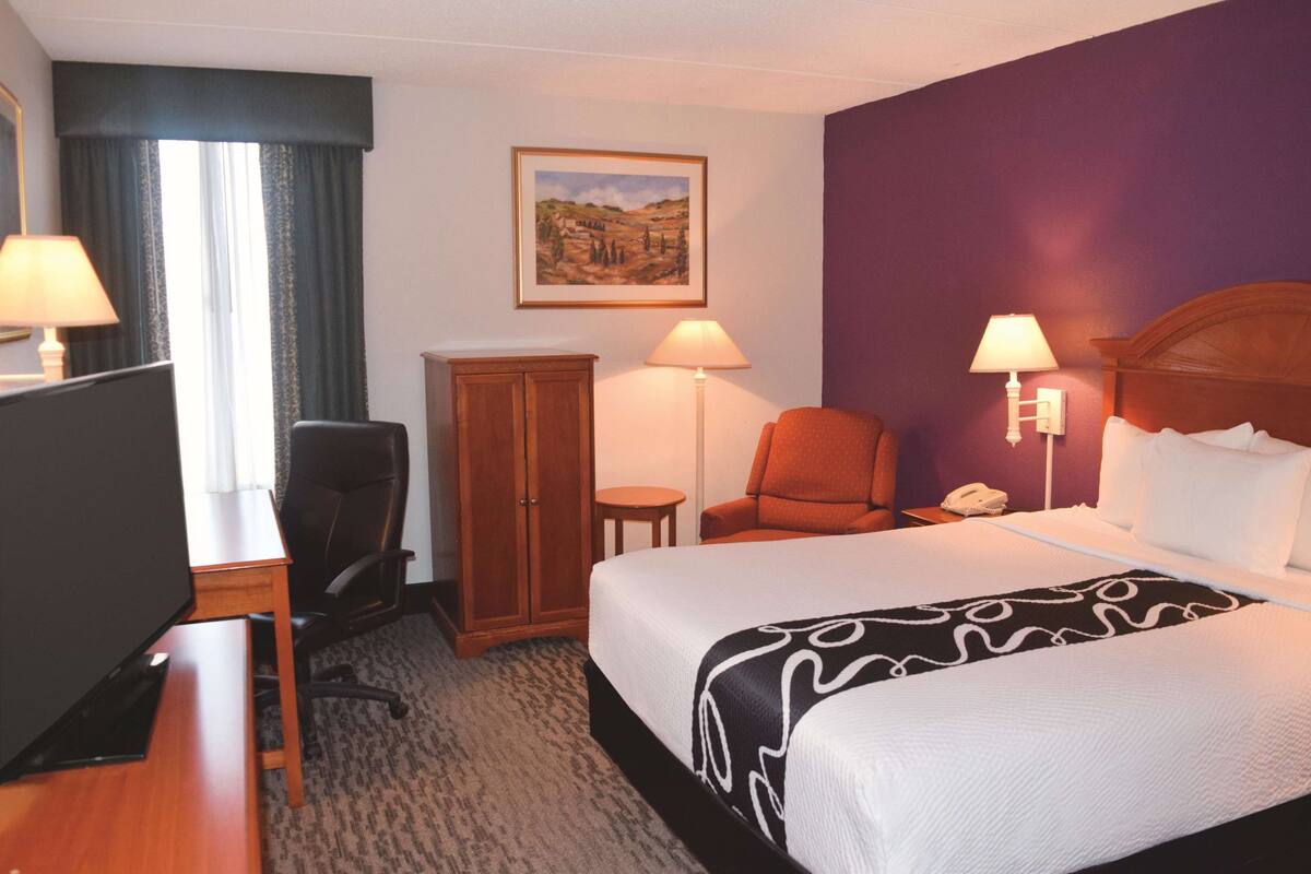 Una habitación de hotel con cama, escritorio, silla y armario.