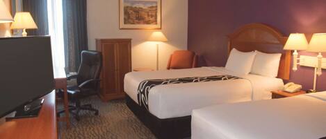 A hotel room with two beds, a desk with a TV, a chair, a lamp, and a painting on the wall.