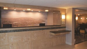 Un área de recepción con pared de azulejos, mostrador y zona de estar con mesas y sillas.