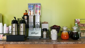 Un comptoir de cuisine avec une machine à café, deux distributeurs de boissons, une cafetière et divers ustensiles de cuisine.