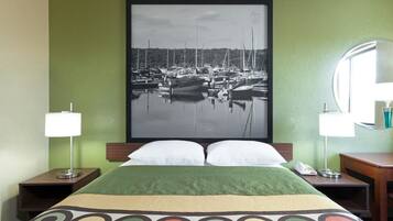 A hotel room with a bed, green walls, a framed photograph of a marina, two bedside lamps, and a round mirror.