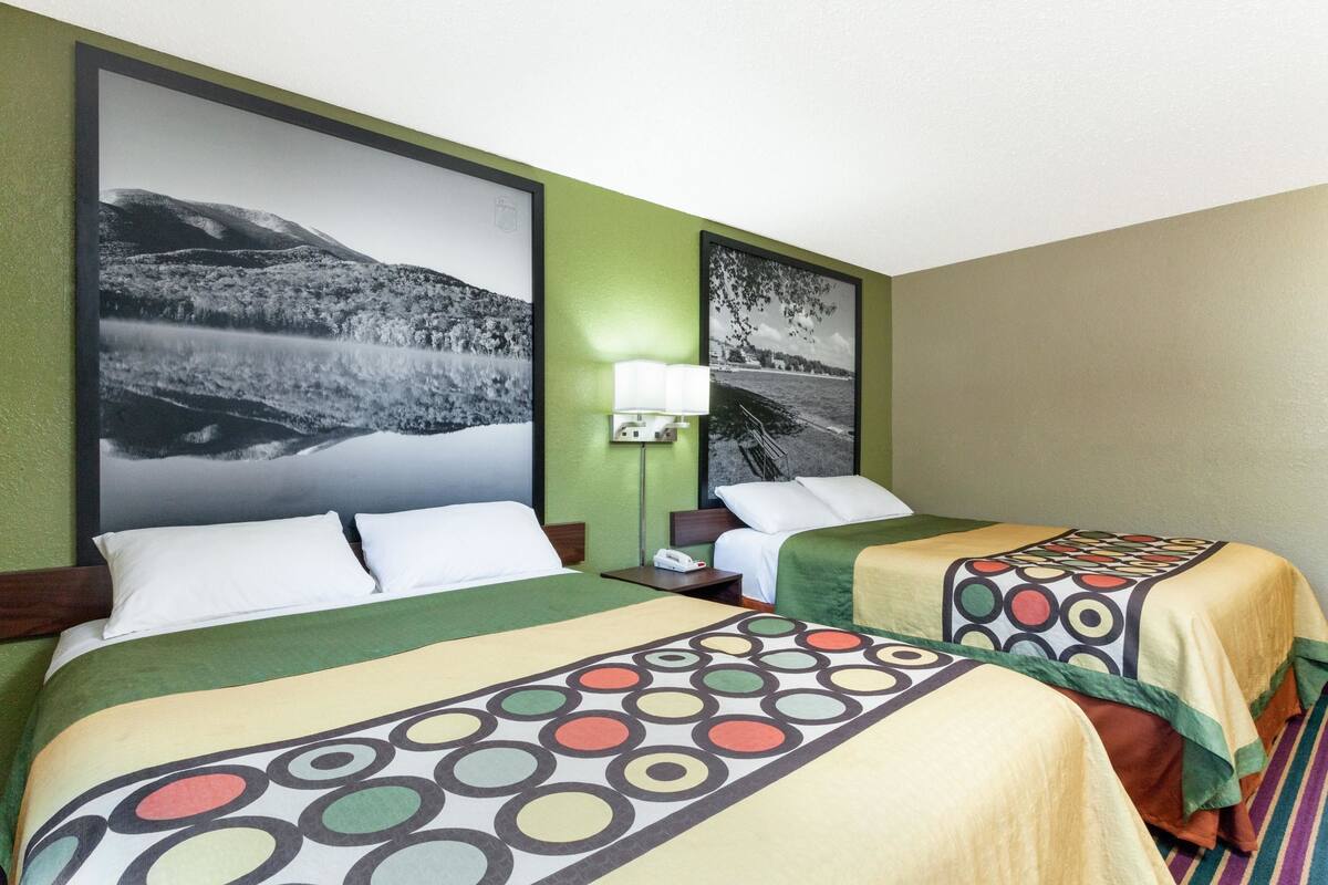 Habitación de hotel con dos camas, paredes verdes y grandes cuadros en blanco y negro de paisajes.