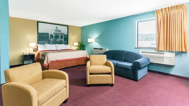 Une chambre d’hôtel comprenant un lit, deux fauteuils, un canapé, une table de chevet, une lampe, une fenêtre avec des rideaux et un climatiseur fixé au mur.