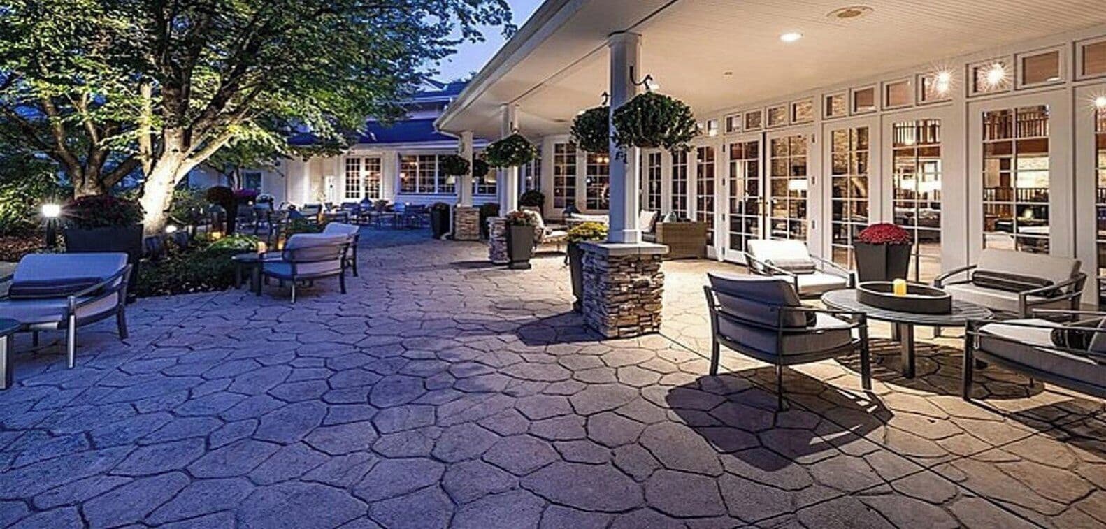 An outdoor patio with hexagonal stone flooring, outdoor seating, and a covered area with large windows.