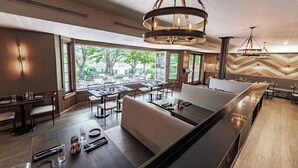 Ein modernes Restaurant mit einem langen Gemeinschaftstisch, gepolsterten Sitzgelegenheiten und großen Fenstern mit Blick ins Freie.