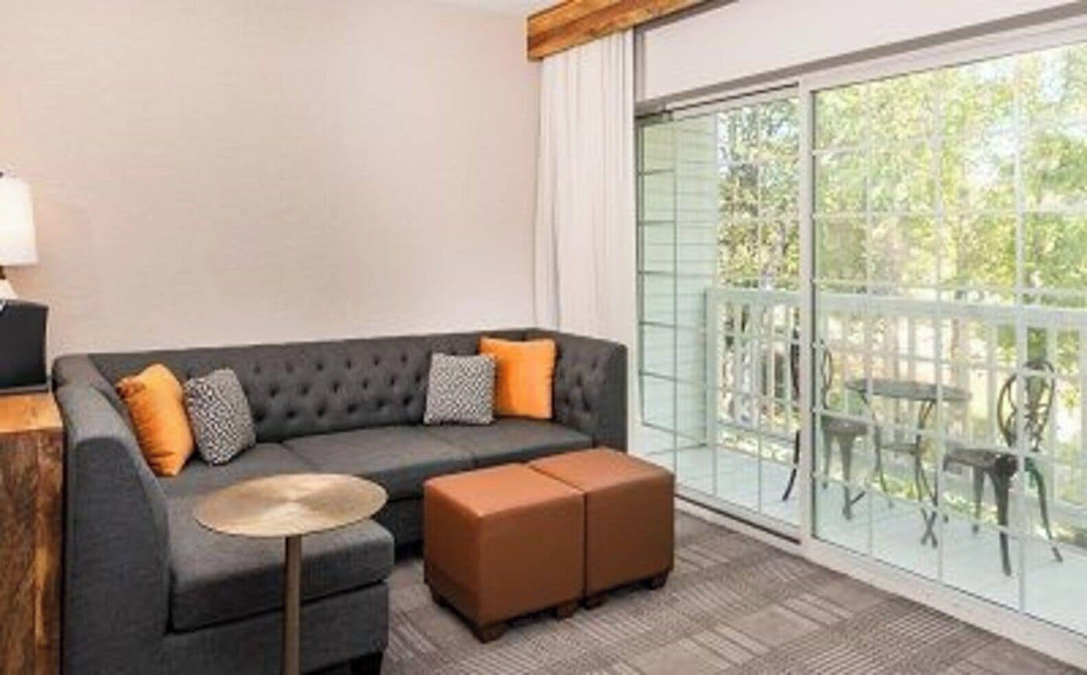 Una sala de estar moderna con un sofá gris, cojines naranja, una mesita redonda y un reposapiés marrón.