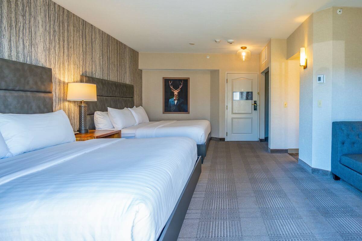 A hotel room with two beds, a headboard, a lamp, a painting, and a door.