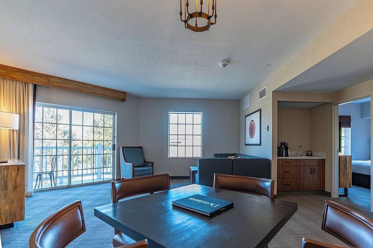 A spacious room with a large dining table, comfortable seating, a kitchen area, and large windows providing natural light.