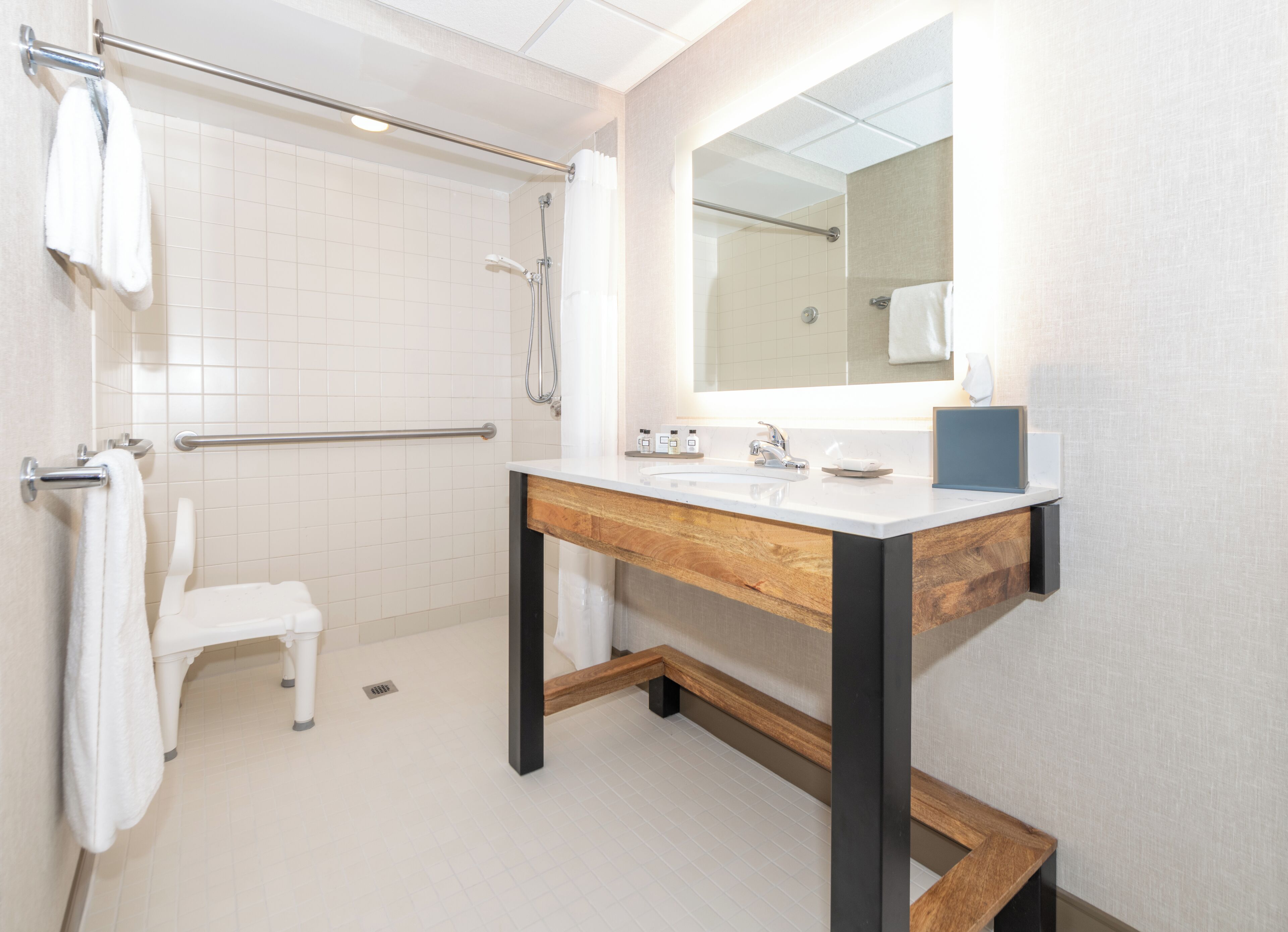 A modern bathroom with a white tiled shower, a wooden vanity with a mirror, and a white toilet.