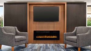Een moderne woonkamer met een flatscreen televisie boven een open haard, twee fauteuils en een kamerkleed met een patroon.