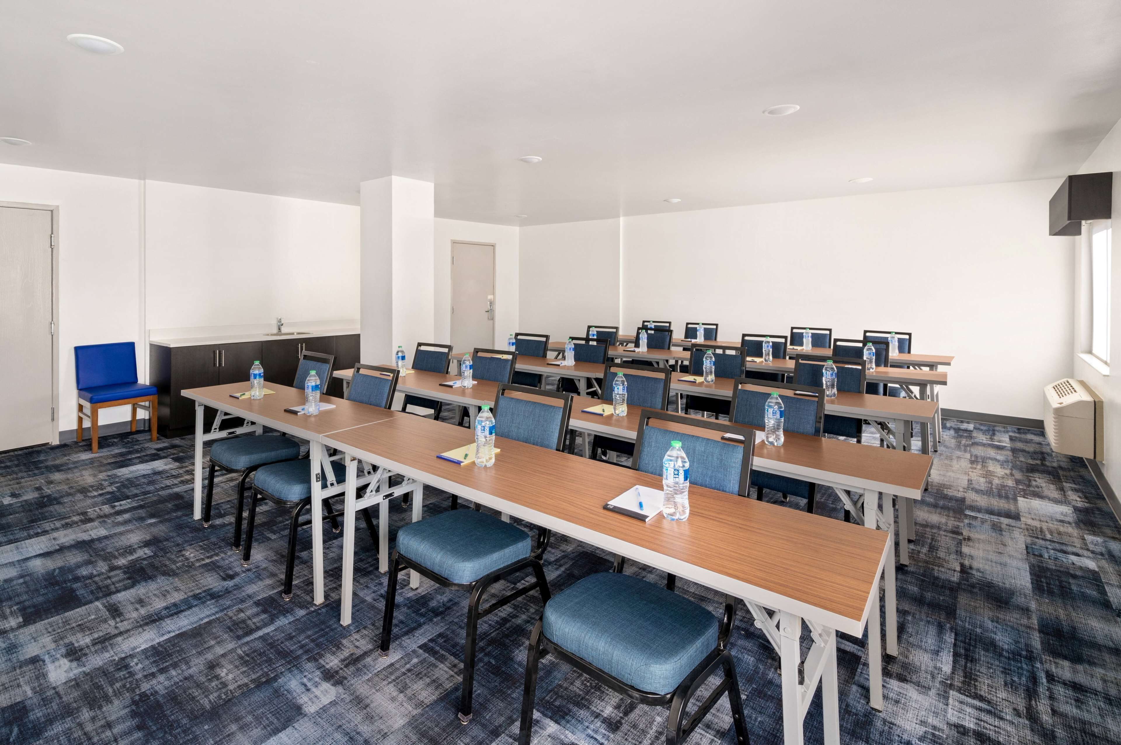 A conference room with multiple tables and chairs, equipped with water bottles and notepads.