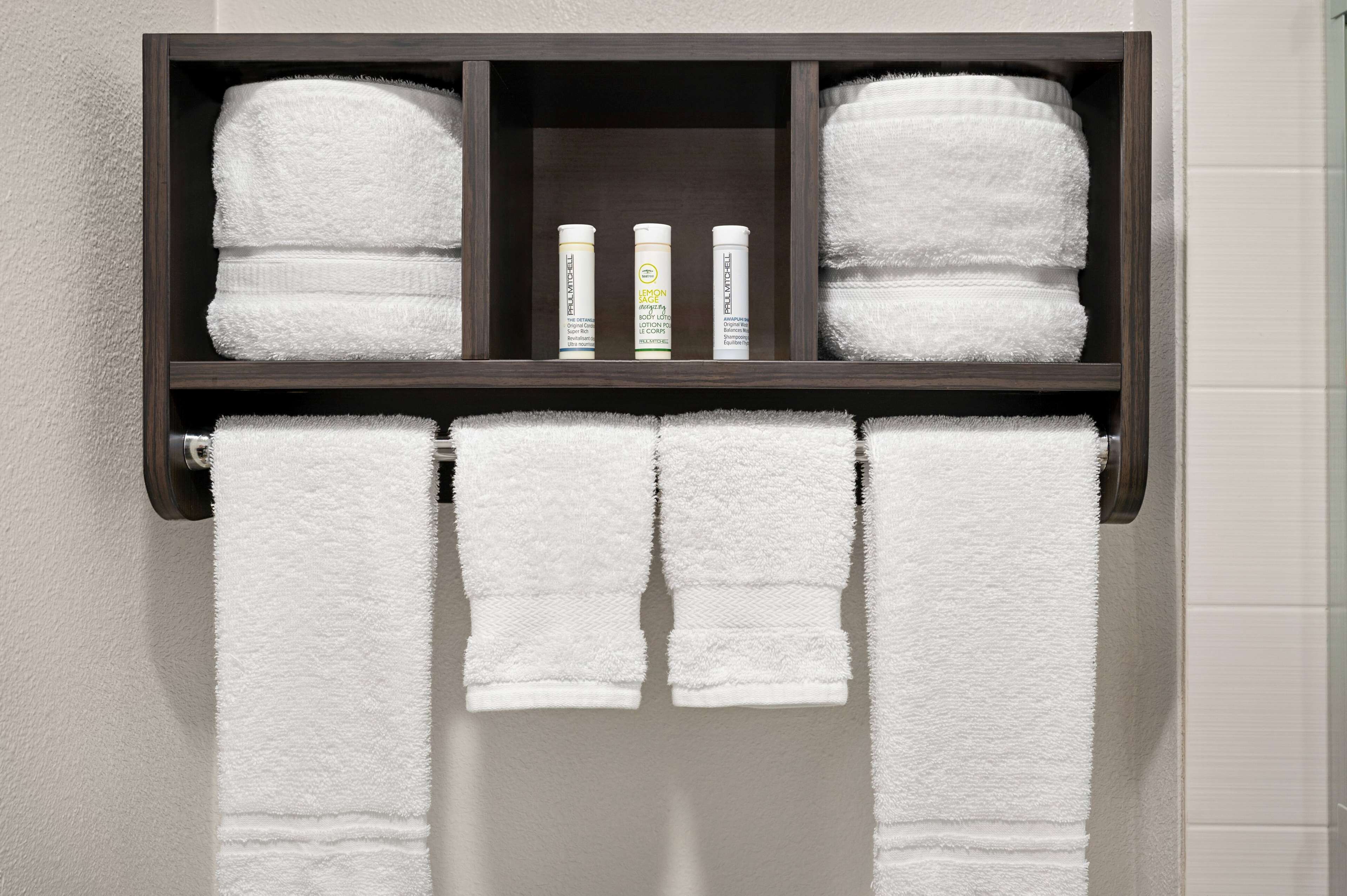 Une salle de bain avec une étagère en bois foncé où sont posés des serviettes blanches et trois flacons de produits de toilette.